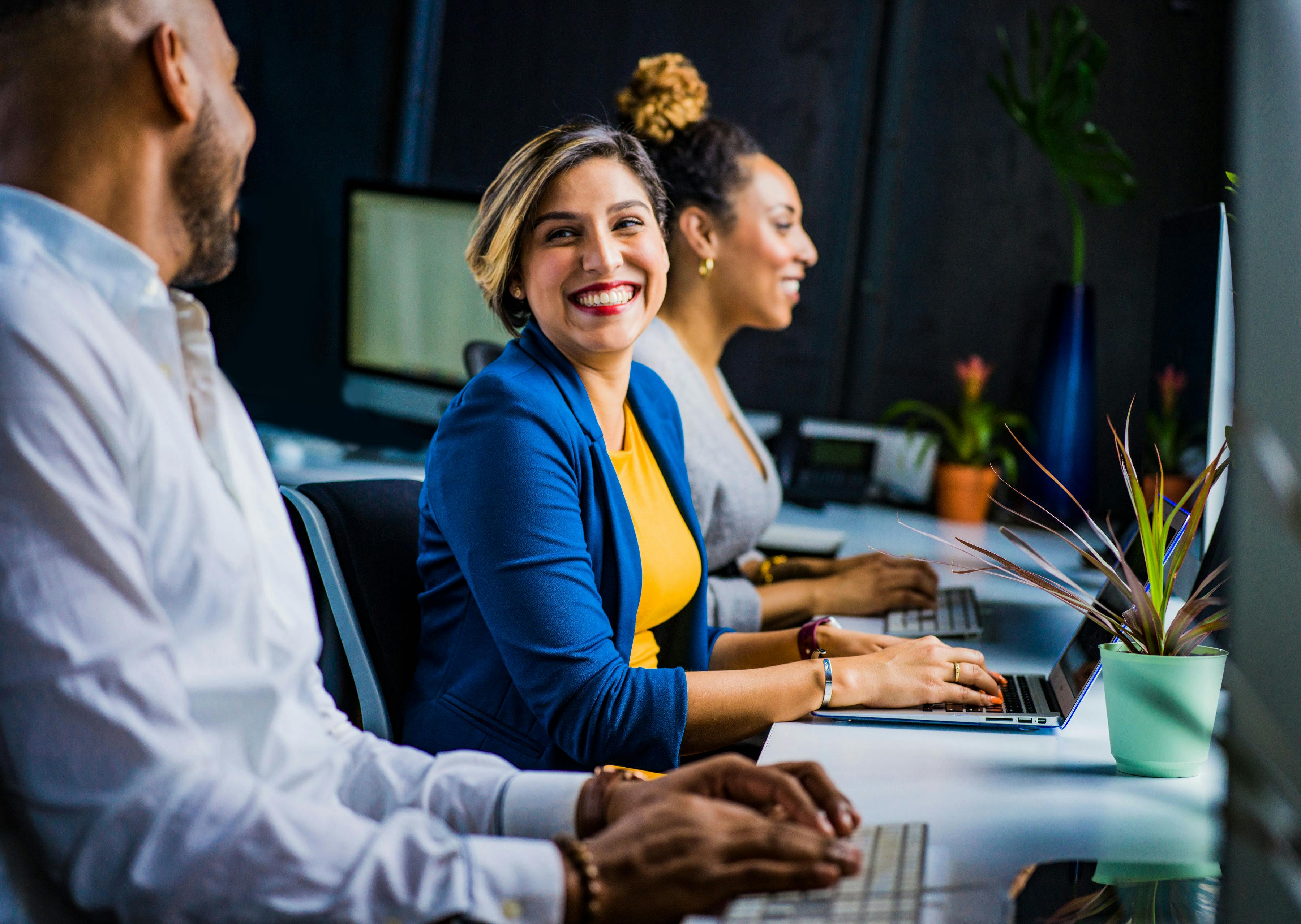 3 people in working in an office, female in blue jacket smiling to their male colleague